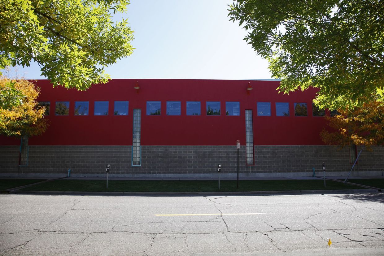 Red building with small windows behind a fence, framed by trees along an empty street.