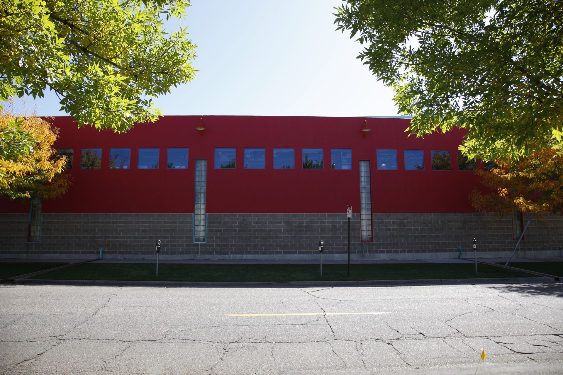 Red building with small windows behind a fence, framed by trees along an empty street.
