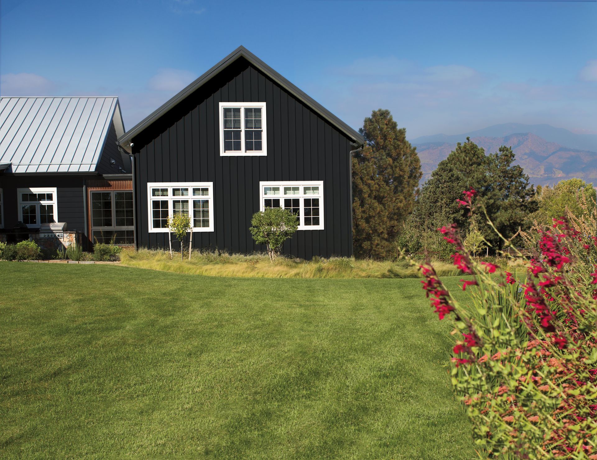 A black house with white windows sits in the middle of a lush green field.
