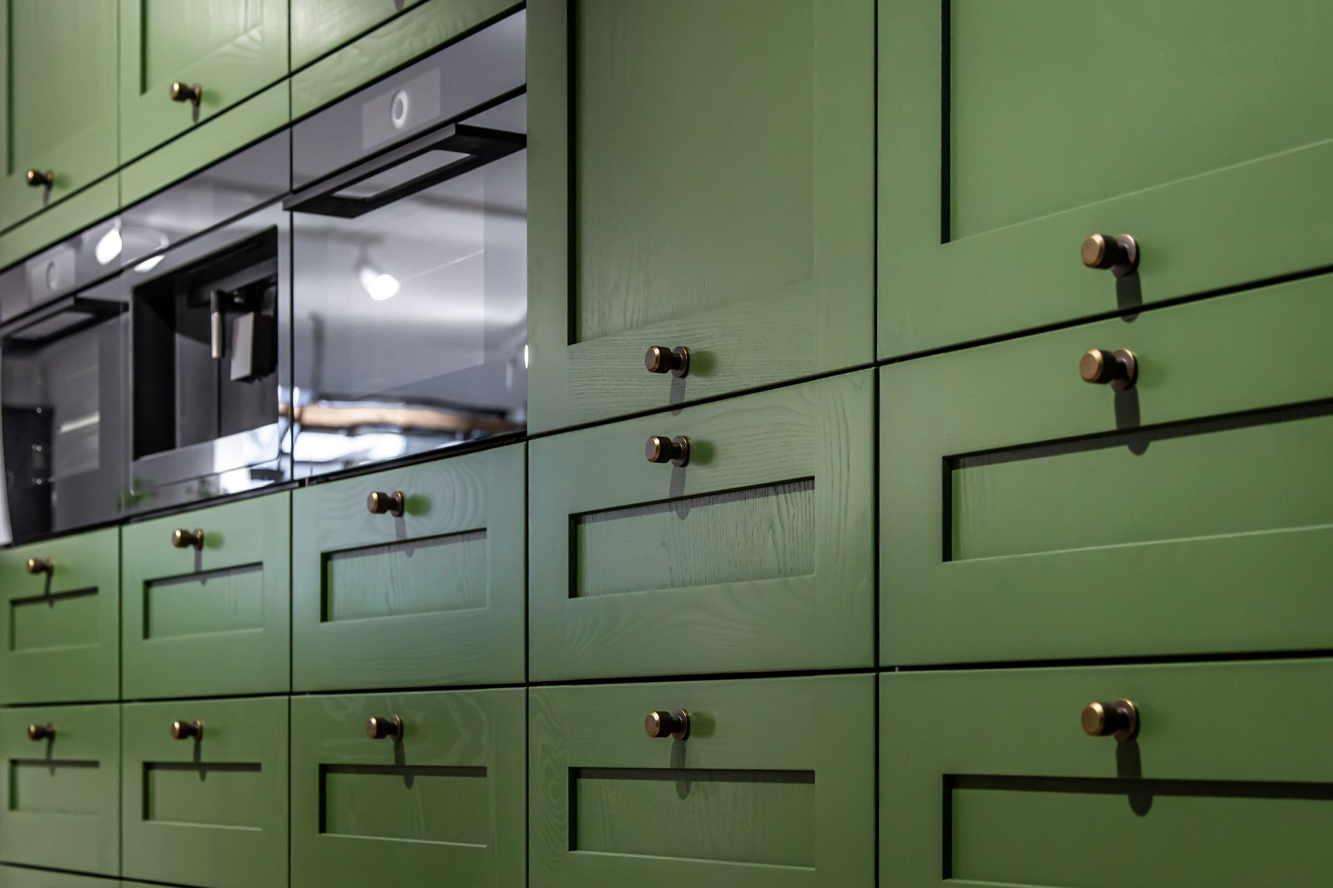 Close-up view of olive green kitchen cabinetry with a built-in oven, microwave, and matching metallic cabinet knobs.