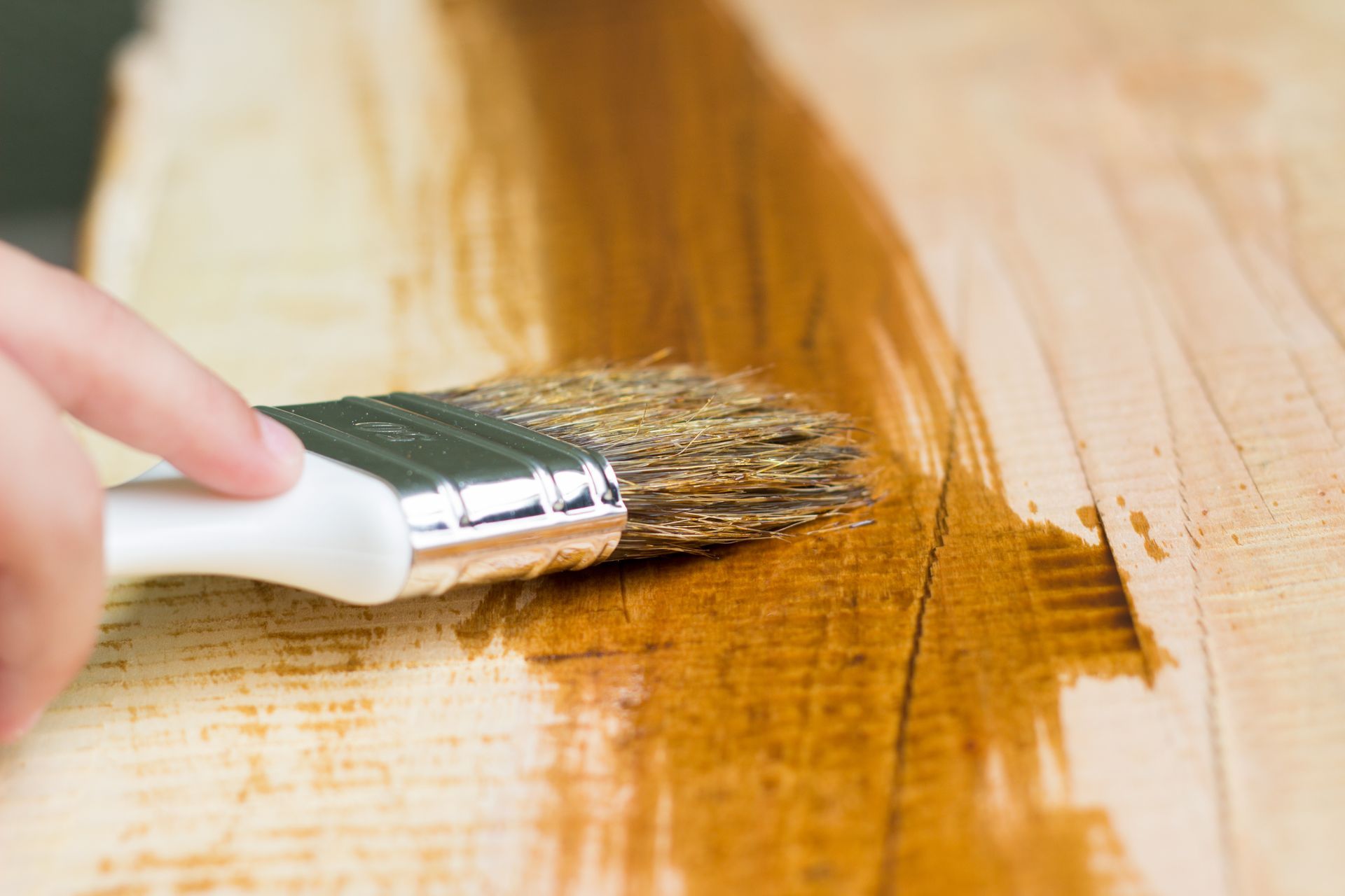 Hand applying wood stain to a wooden surface with a brush.