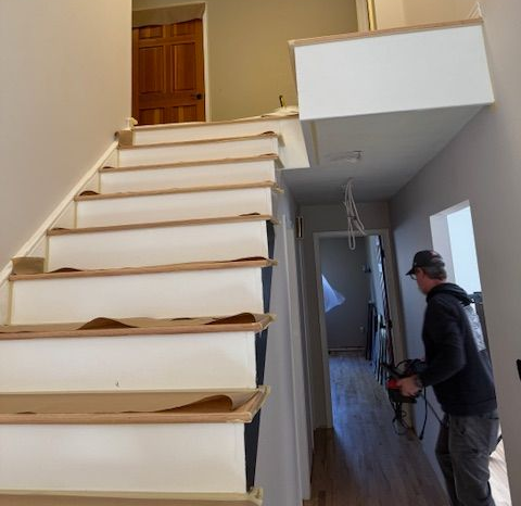 Interior stairwell with unfinished steps, a loft landing, and a worker holding tools at the bottom.
