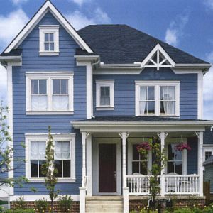 Blue two-story house with white trim, dark roof, and small front porch under a partly cloudy sky.