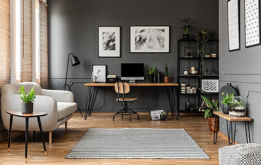 Modern home office with desk, computer, chair, gray walls, plants, and a striped rug