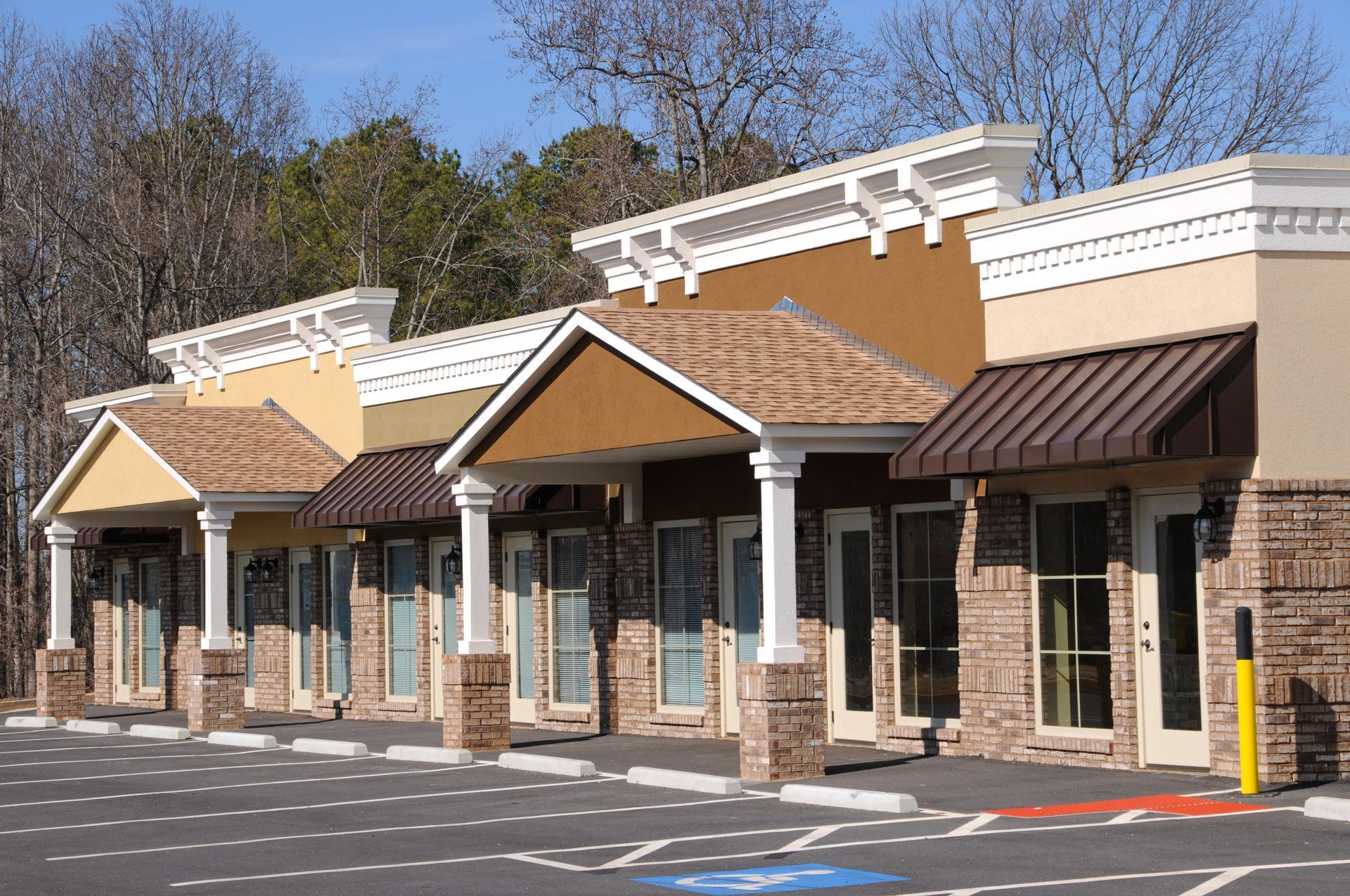Strip mall with various colored facades, awnings, and columns in front of a parking lot.