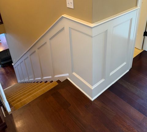 Interior staircase with white wainscoting, beige walls, and dark wood floors.