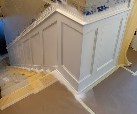 Staircase and wall paneling under renovation, covered in plastic sheeting and painter’s tape