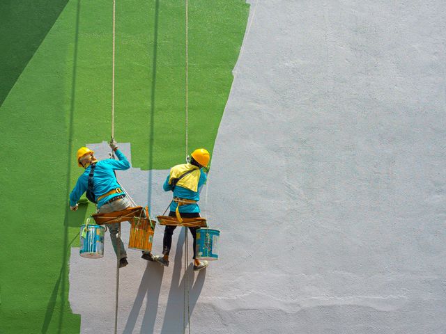 two workers are painting a wall on a rope