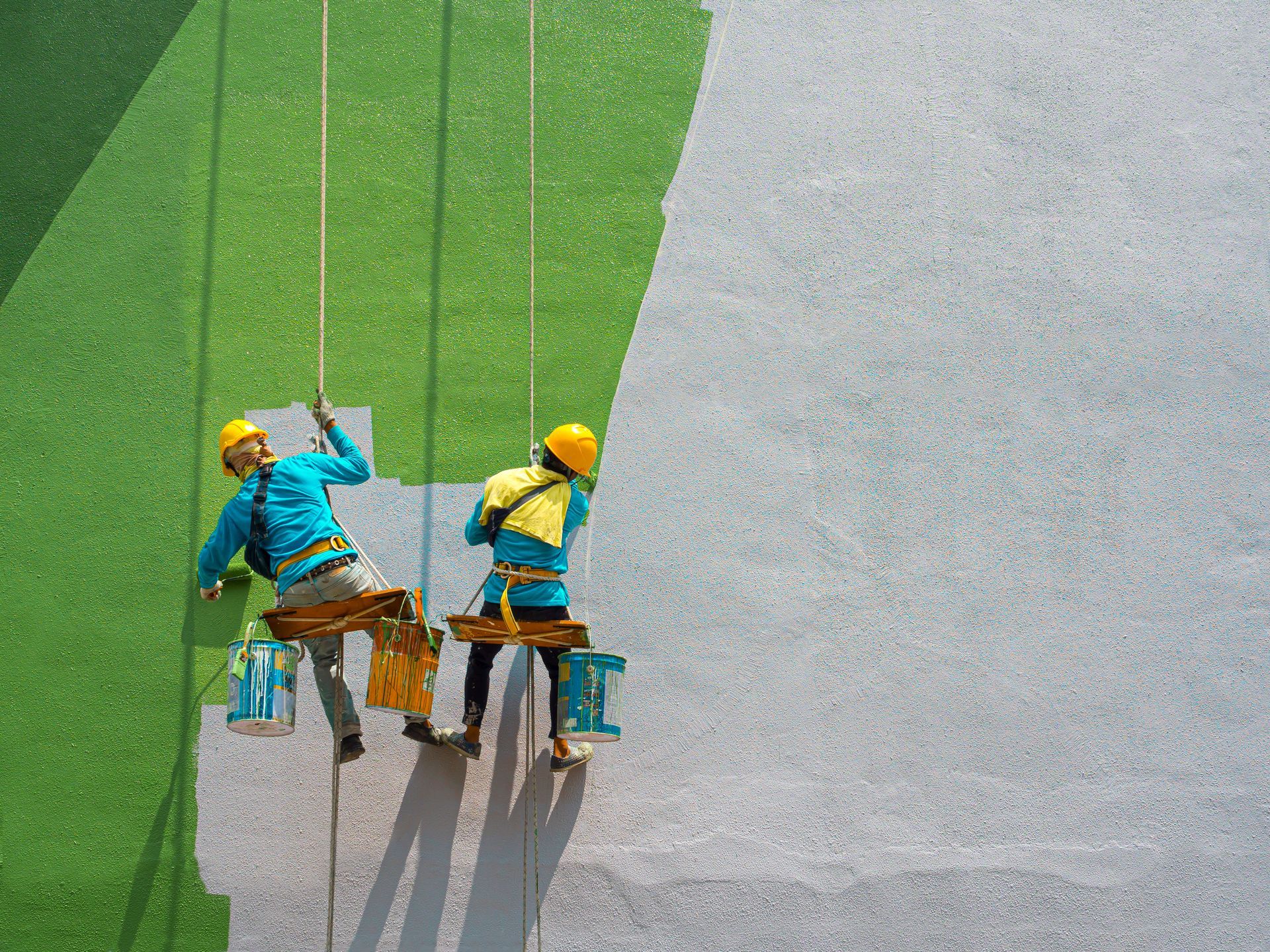 Two men are painting a wall on a rope.