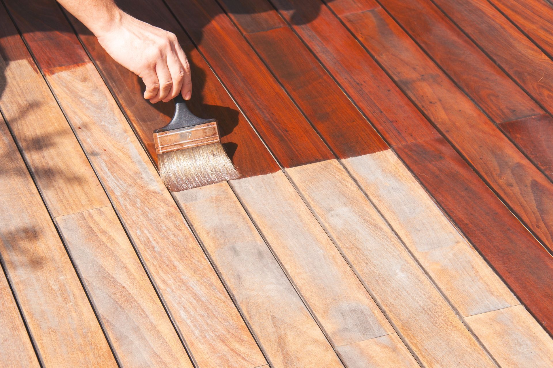 A person is painting a wooden deck with a brush.