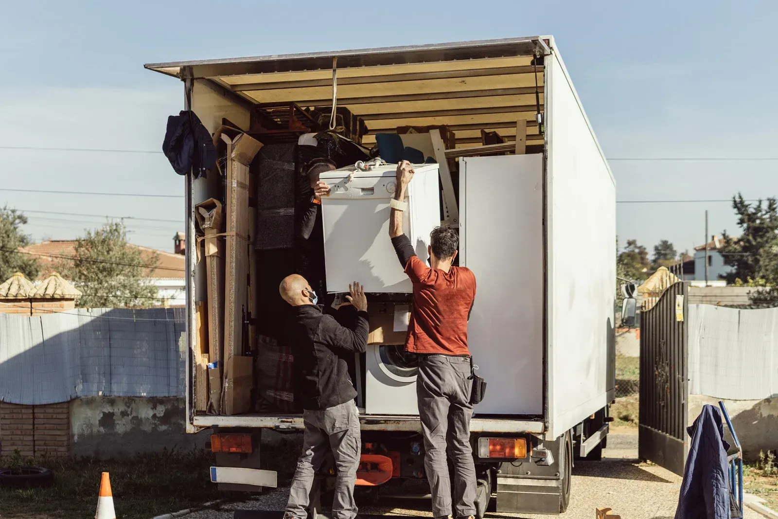 Movers loading appliances into a white moving truck under a clear sky.