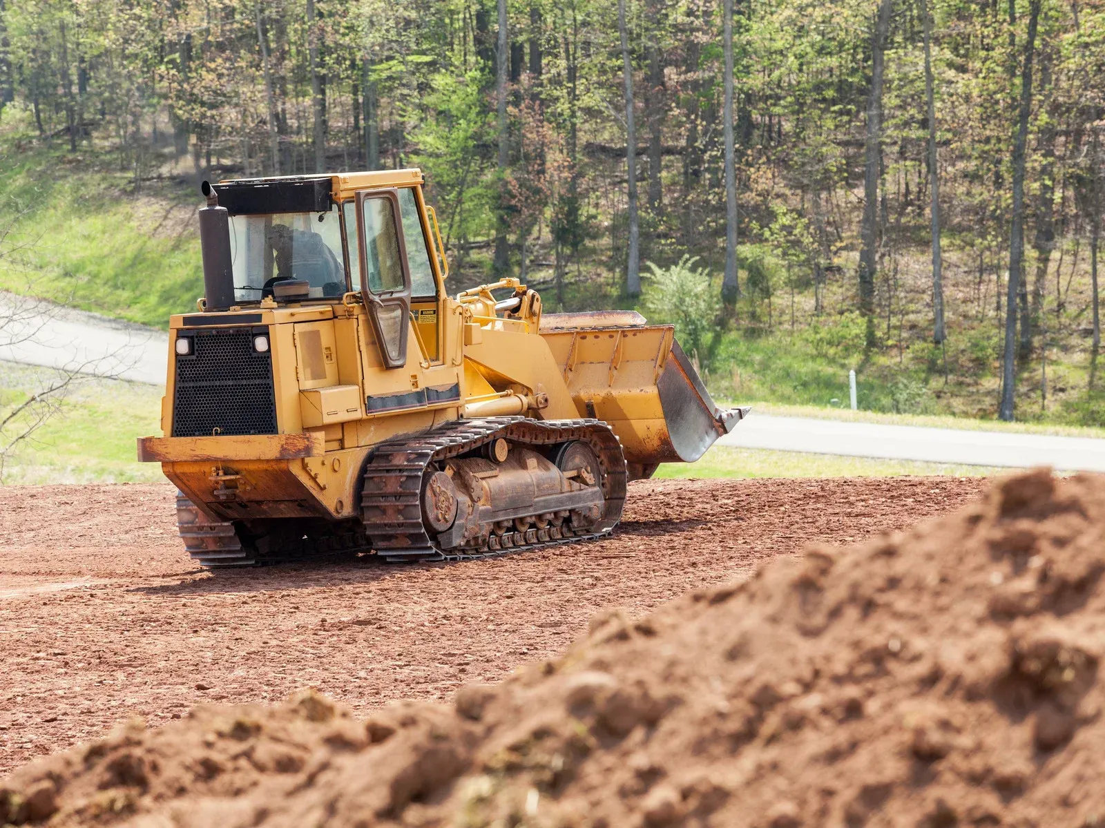 Yellow bulldozer on muddy ground, clearing land near trees.