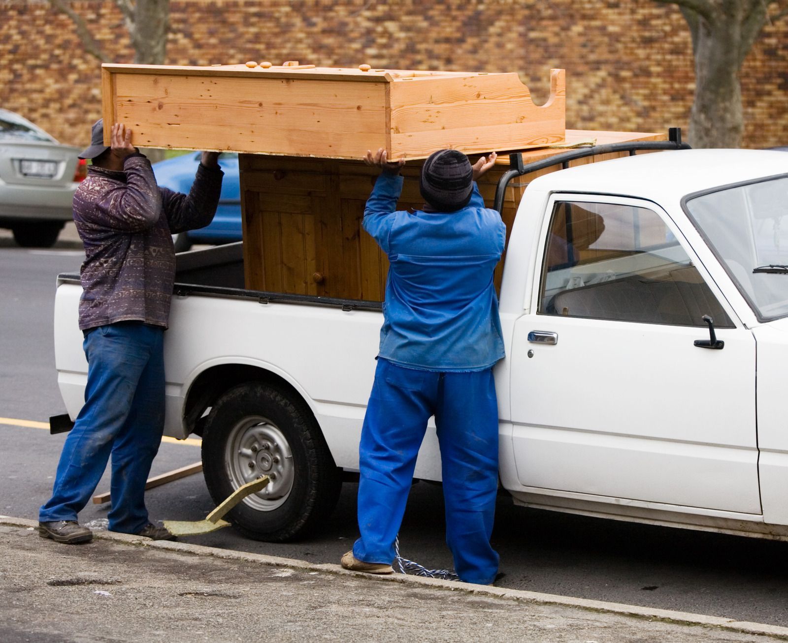 Two people loading furniture into a moving truck via a ramp; one person walks up the ramp.