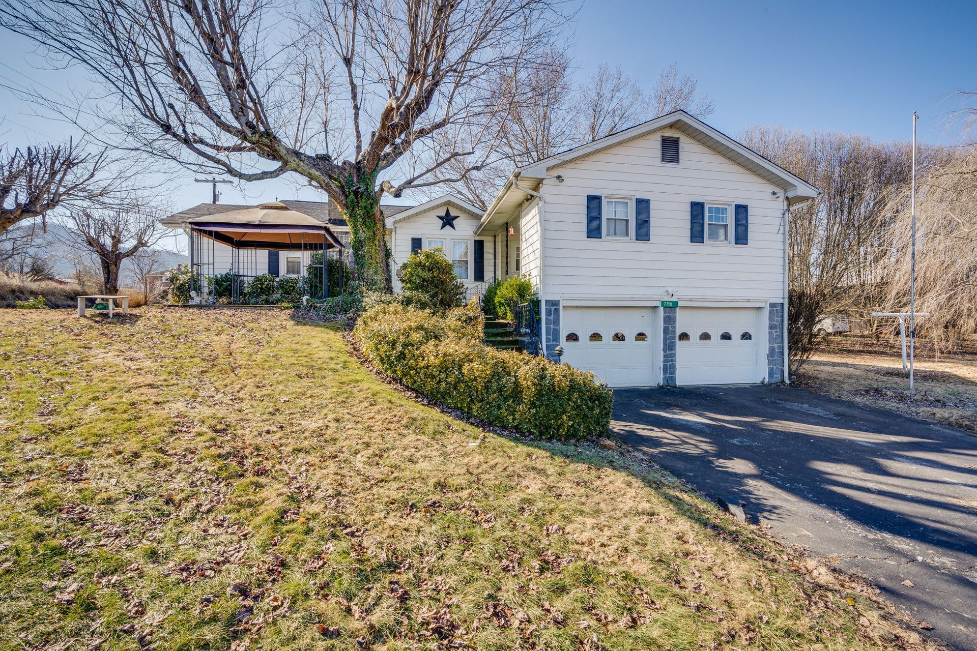 White house with two-car garage, blue shutters, and covered outdoor space. Autumn scene.