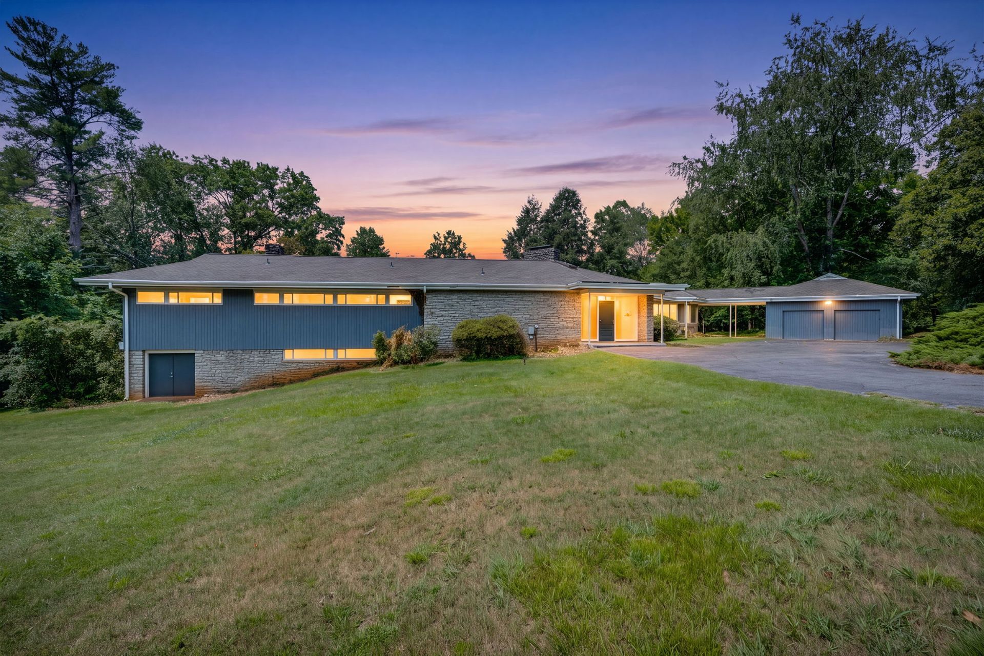 Single-story house at dusk with lit windows, attached garage, and a grassy front yard.