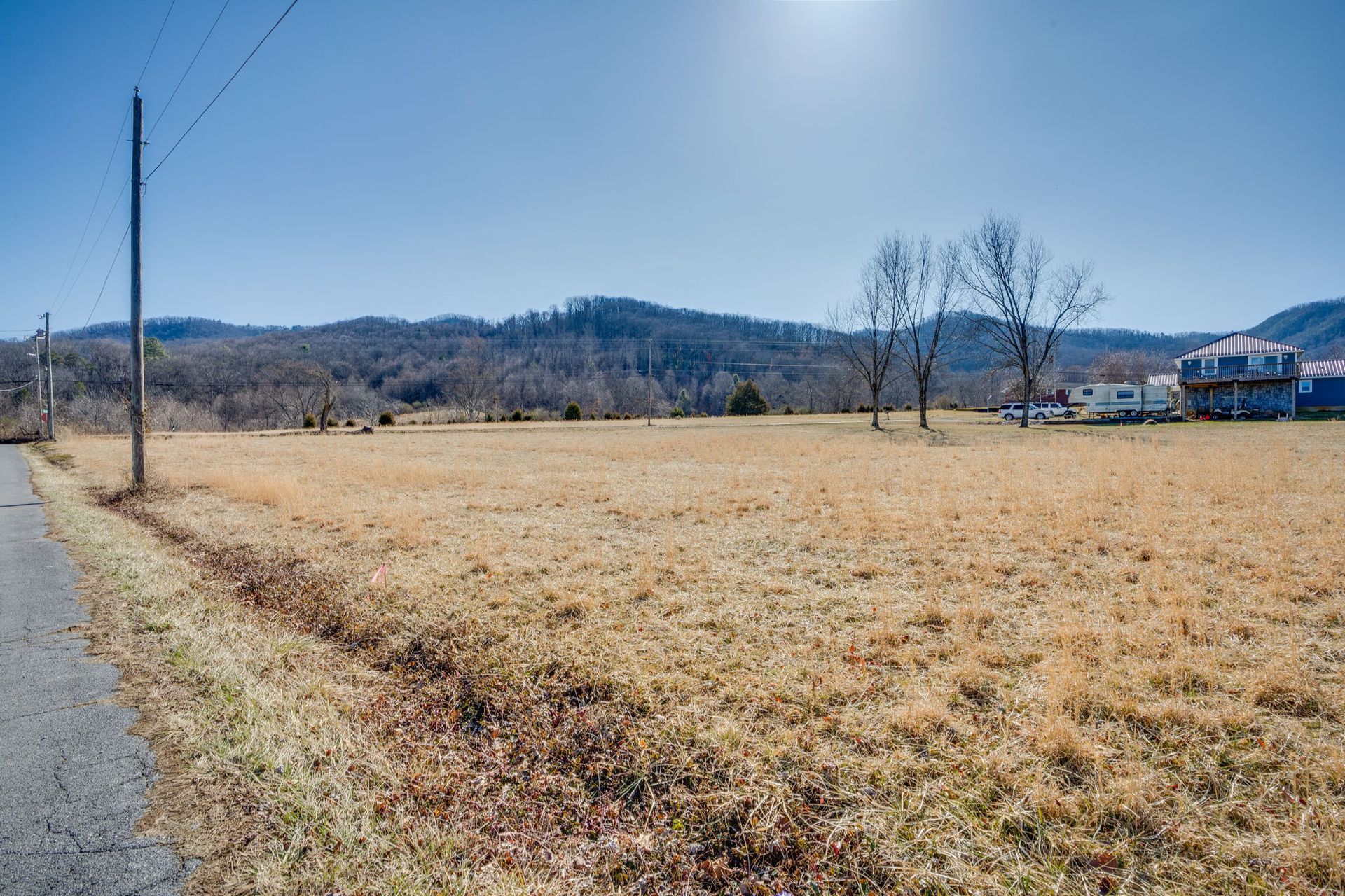Open field of dry grass with power lines and distant mountains under a sunny sky.