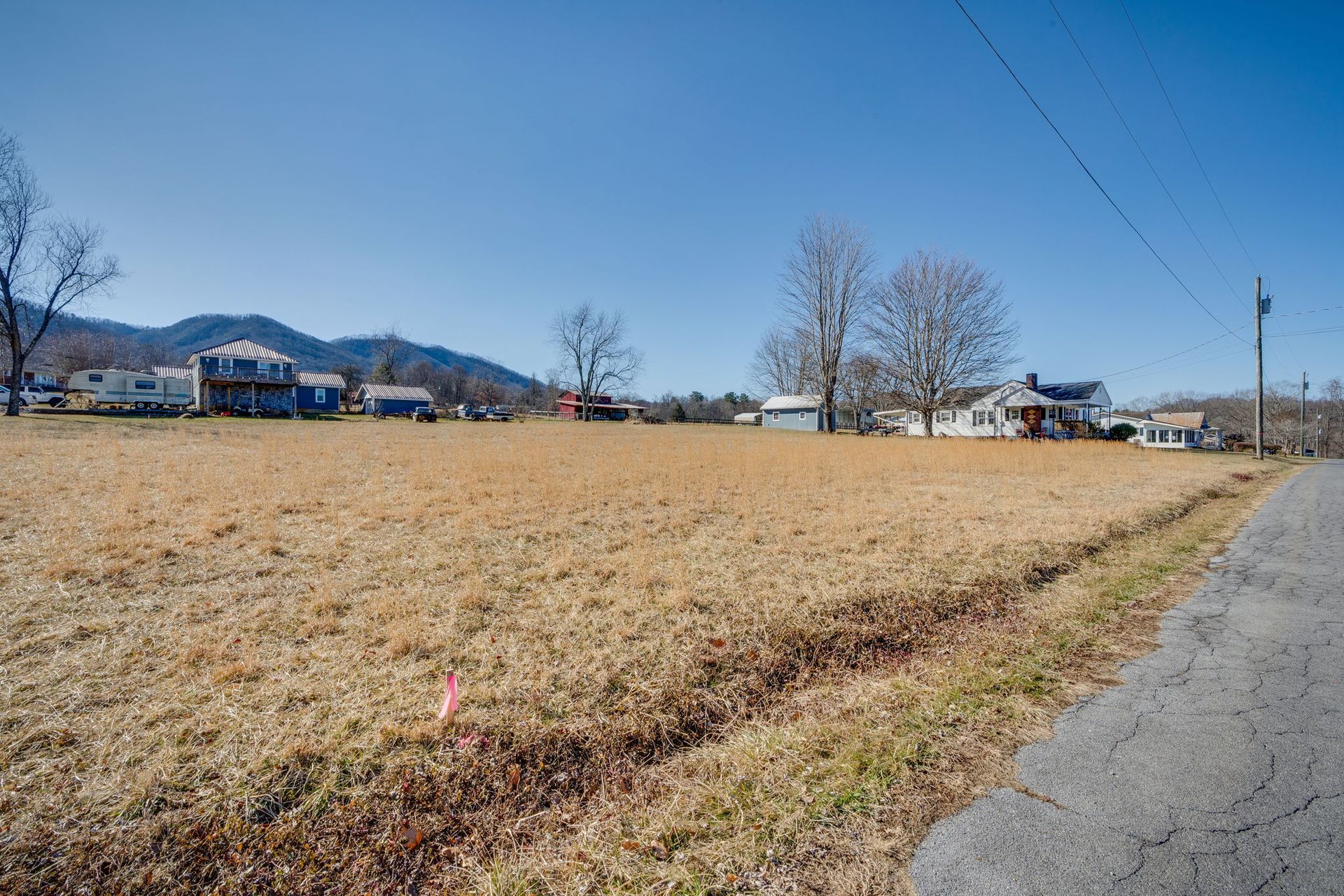 Open field with brown grass, houses in the distance, and blue sky.