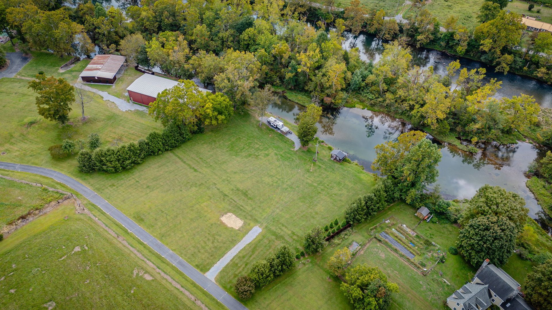 Aerial view of a grassy property with a river, trees, and buildings.