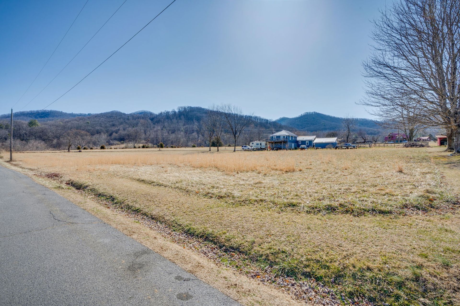 Open field next to a road, with a house in the distance and mountains in the background. Sunny day.
