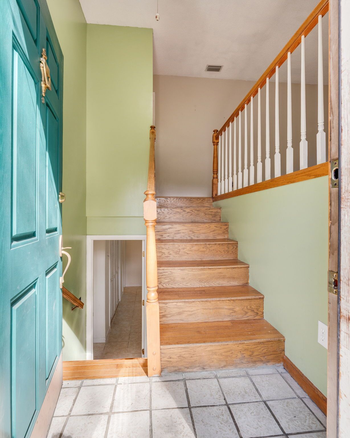 A foyer featuring a teal door, tiled floor, pale green walls, and a wood staircase leading to an upper level.