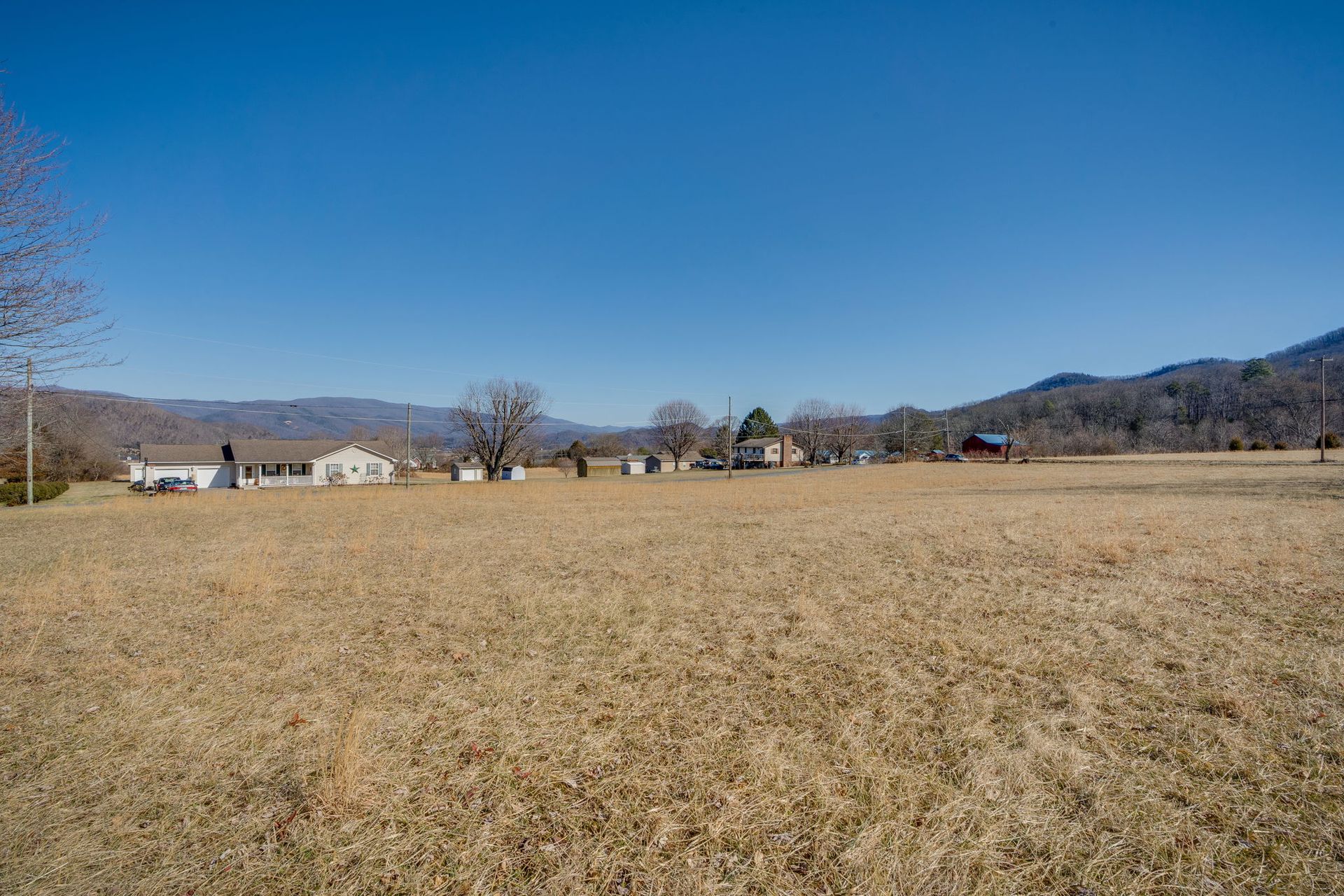 Brown field with buildings and mountains under a blue sky.