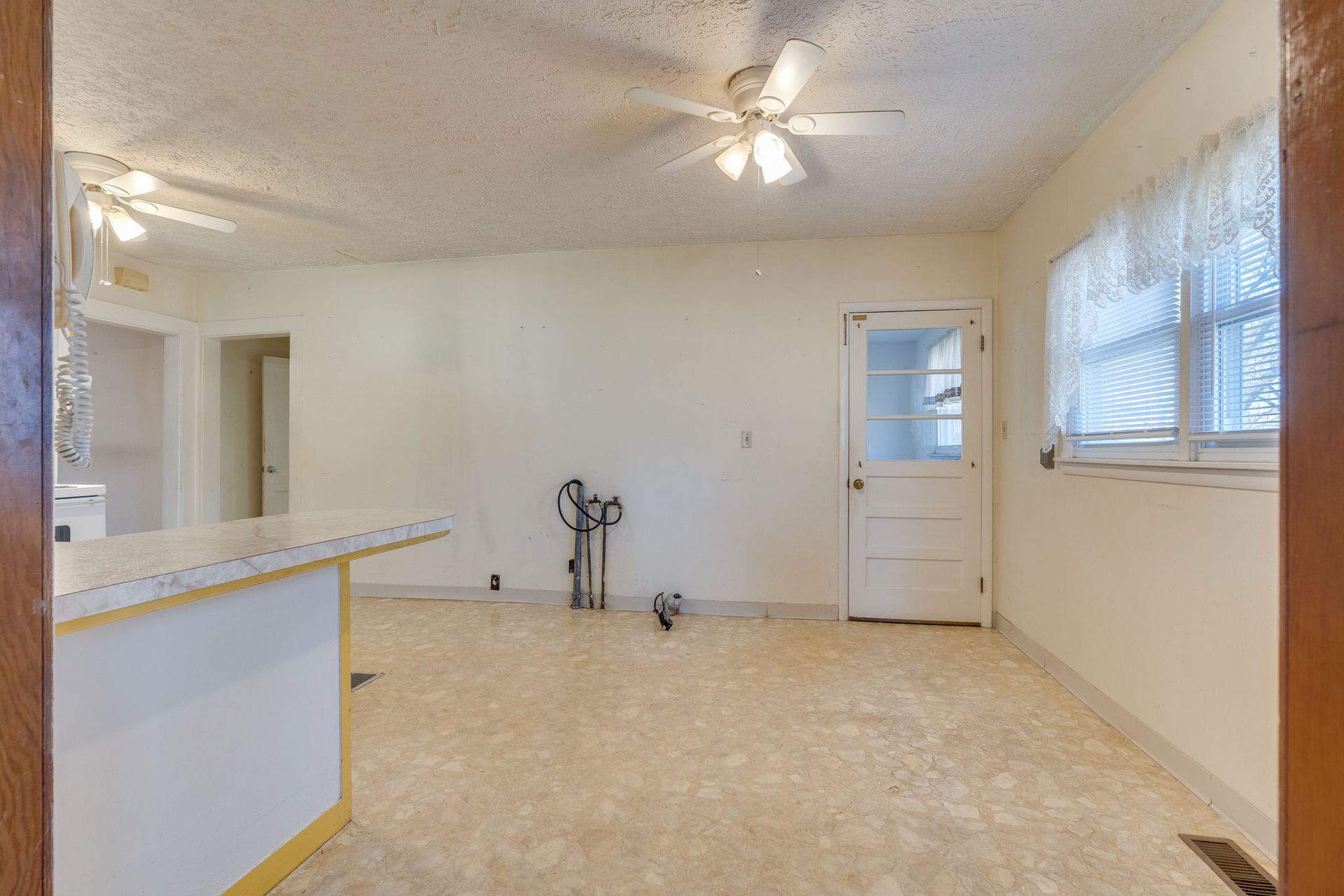 Empty room with cream walls, ceiling fans, and a door, seen from a doorway; a breakfast bar is on the left.