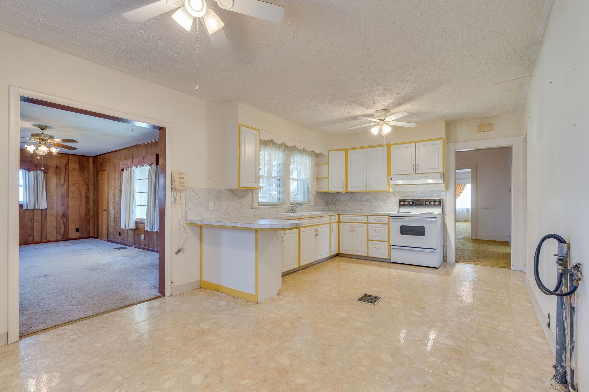 Kitchen with white cabinets, linoleum floor, and a view into a wood-paneled room.