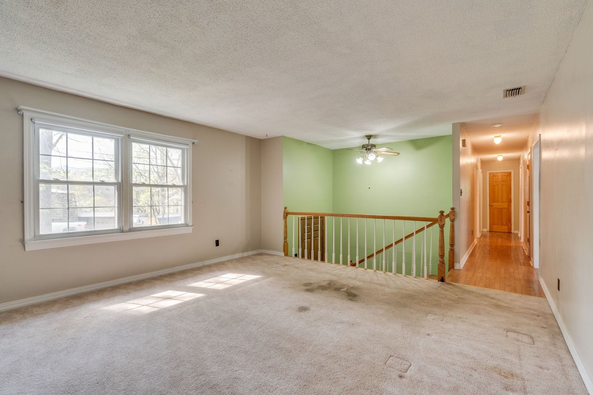 An upstairs room featuring beige carpet, light walls, a green accent wall, wooden stair railings, and a hallway.