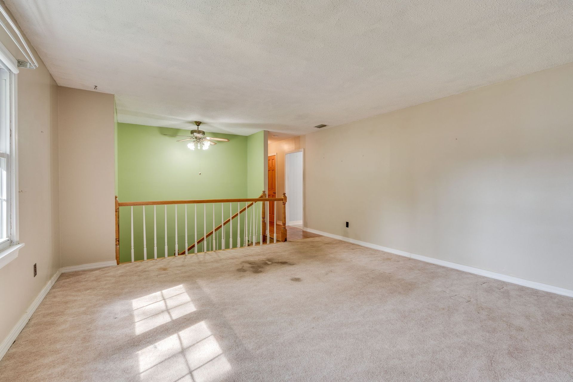 An upstairs room with beige carpet, light walls, a green accent wall, and a staircase with a wooden railing.