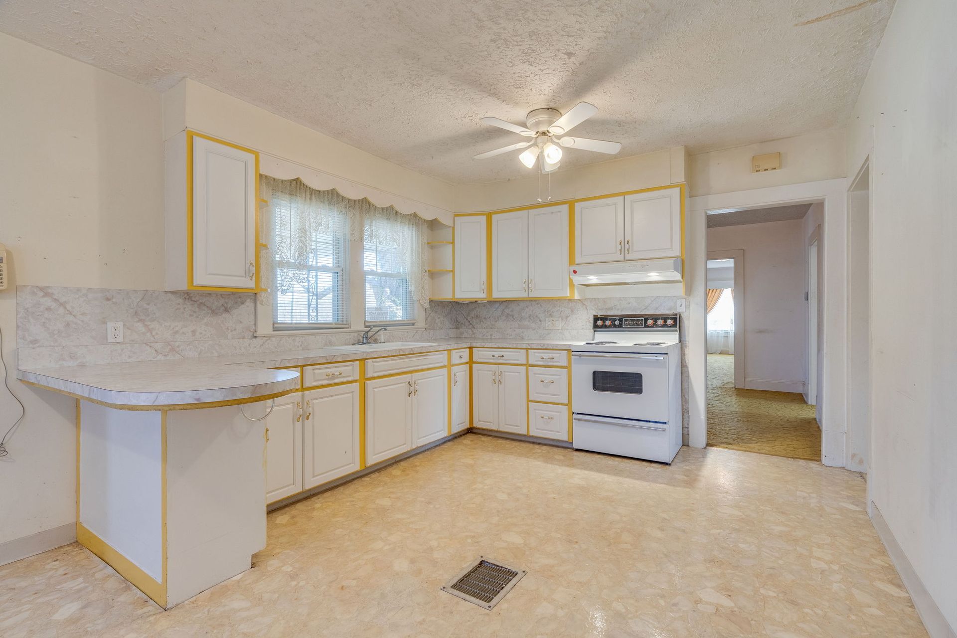 White kitchen with yellow trim, cabinets, and appliances. Vinyl flooring, small window, doorway.