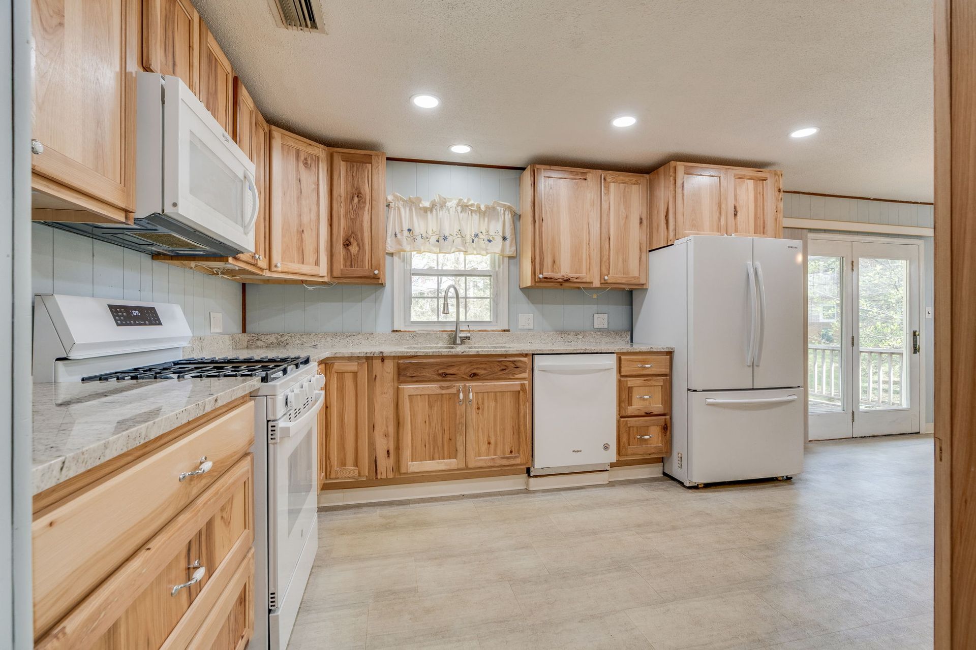 Kitchen featuring light wood cabinets, granite countertops, white appliances, and a window above the sink.