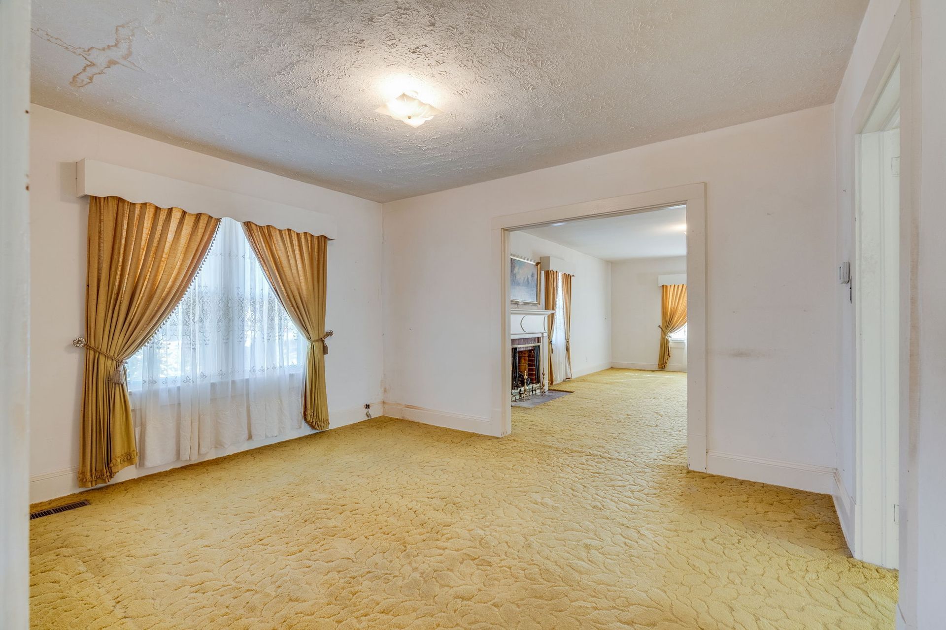 Empty living room with yellow carpet, curtains, and an archway to another room.