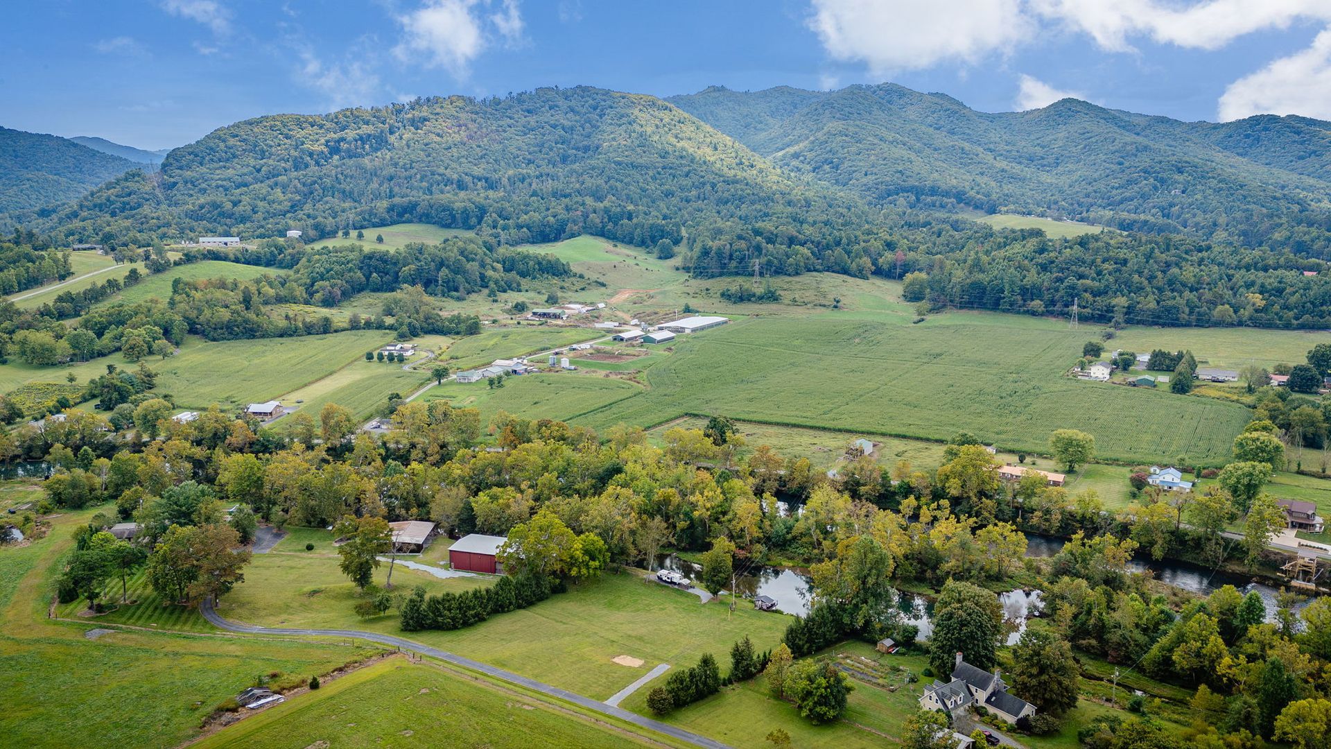 Green valley with buildings, river, and mountain backdrop under blue sky.
