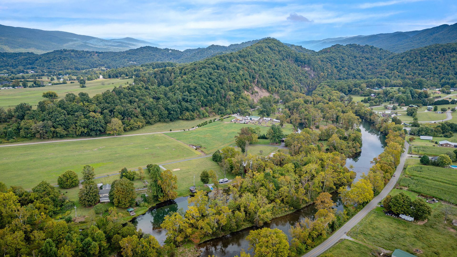 River winding through a valley with green fields, trees, and a distant mountain range.
