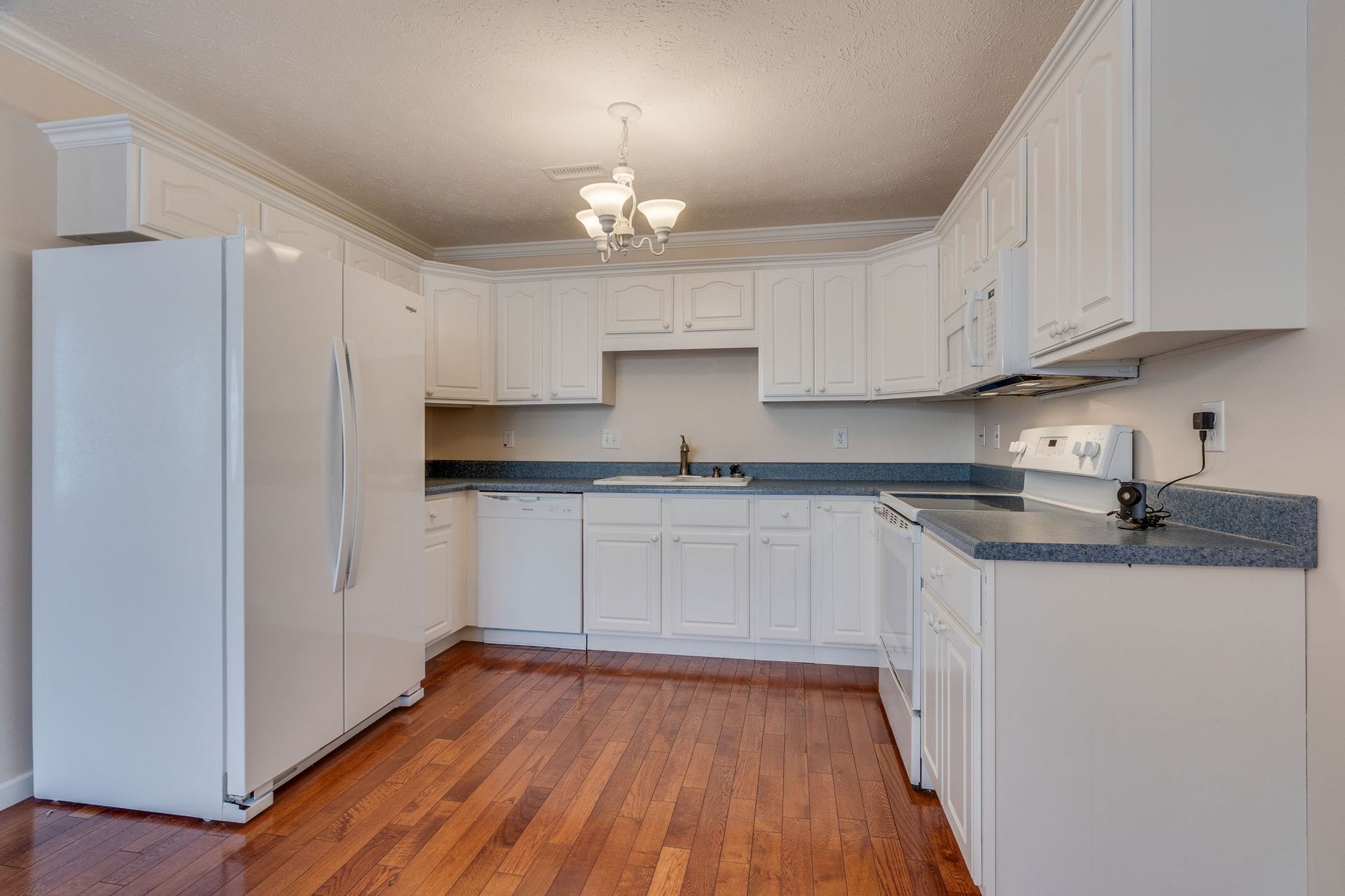 A kitchen with white cabinets, light-colored countertops, a white refrigerator, and hardwood flooring.
