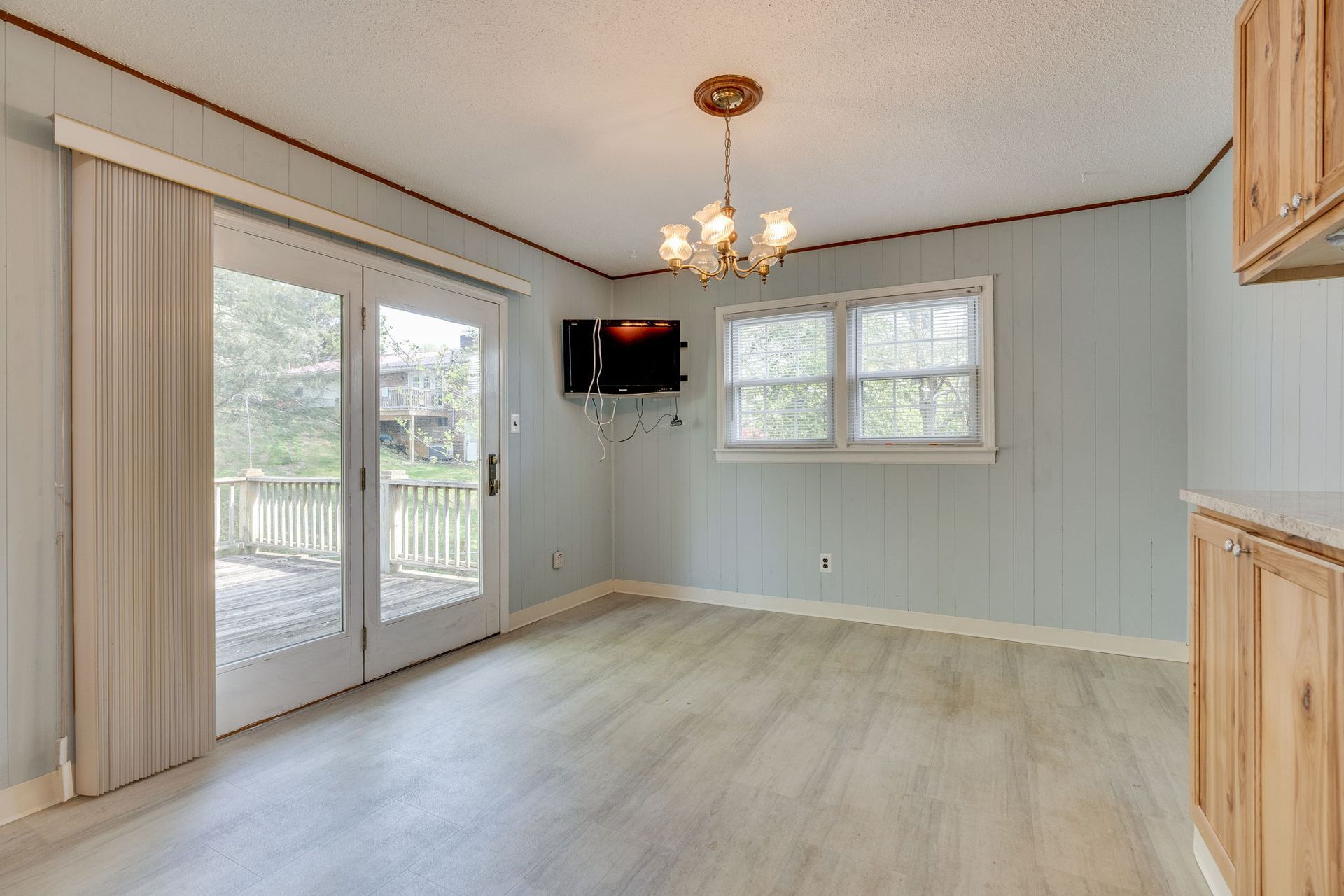 A bright dining area with light wood-look flooring, light blue walls, a floral chandelier, and sliding glass patio doors.