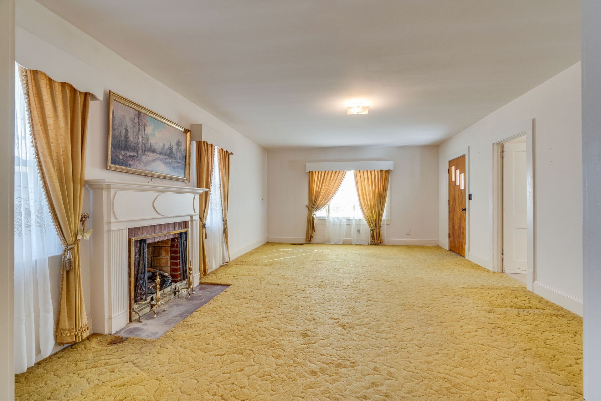 Empty room with yellow carpet, curtains, and fireplace.