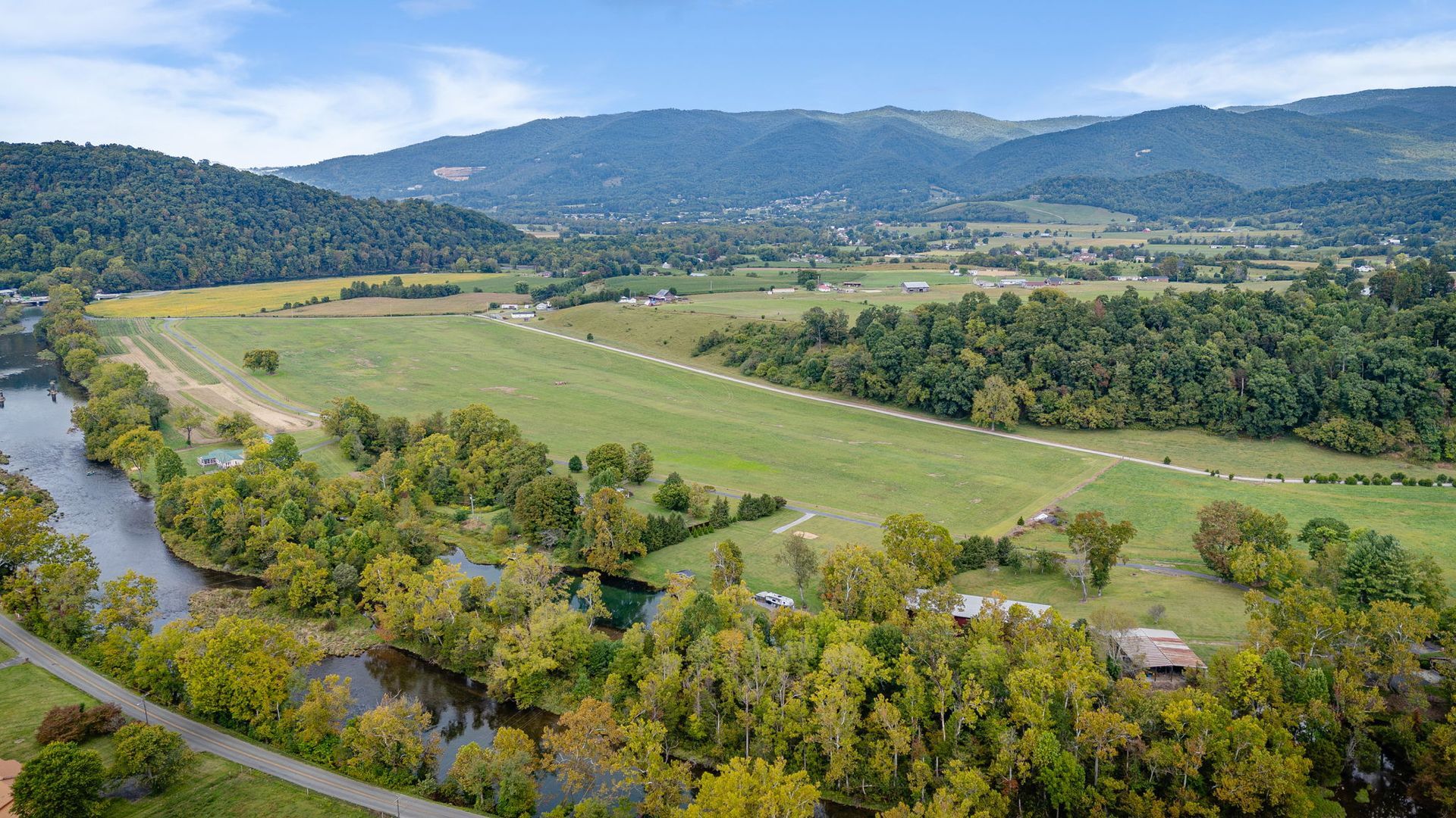 Aerial view of a green field with a river, trees, and mountains in the background.