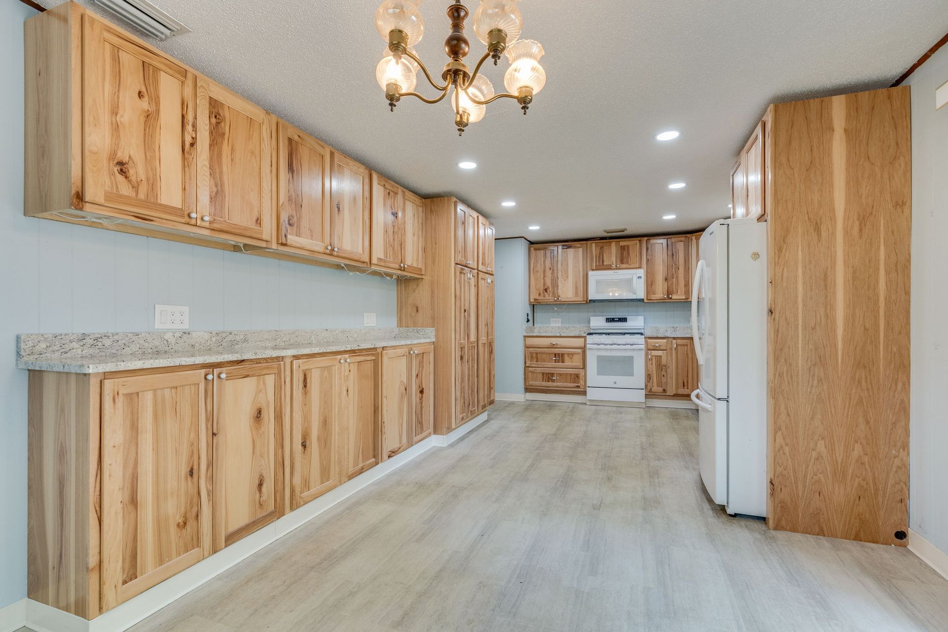 A spacious kitchen featuring light wood cabinets, granite countertops, stainless steel appliances, and wood-look flooring.