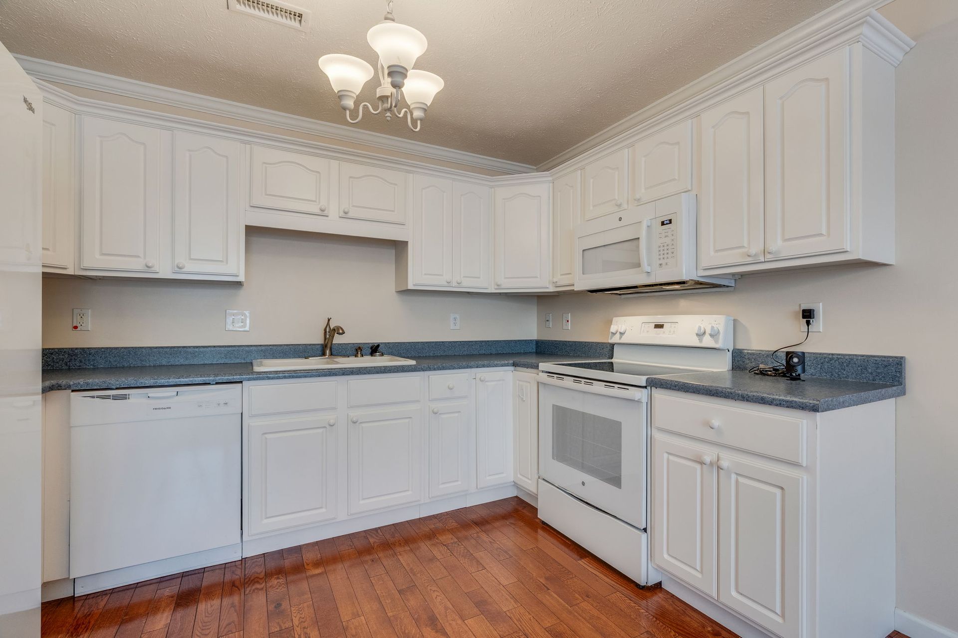 A white kitchen with wooden floors, blue countertops, and white appliances under a modern light fixture.