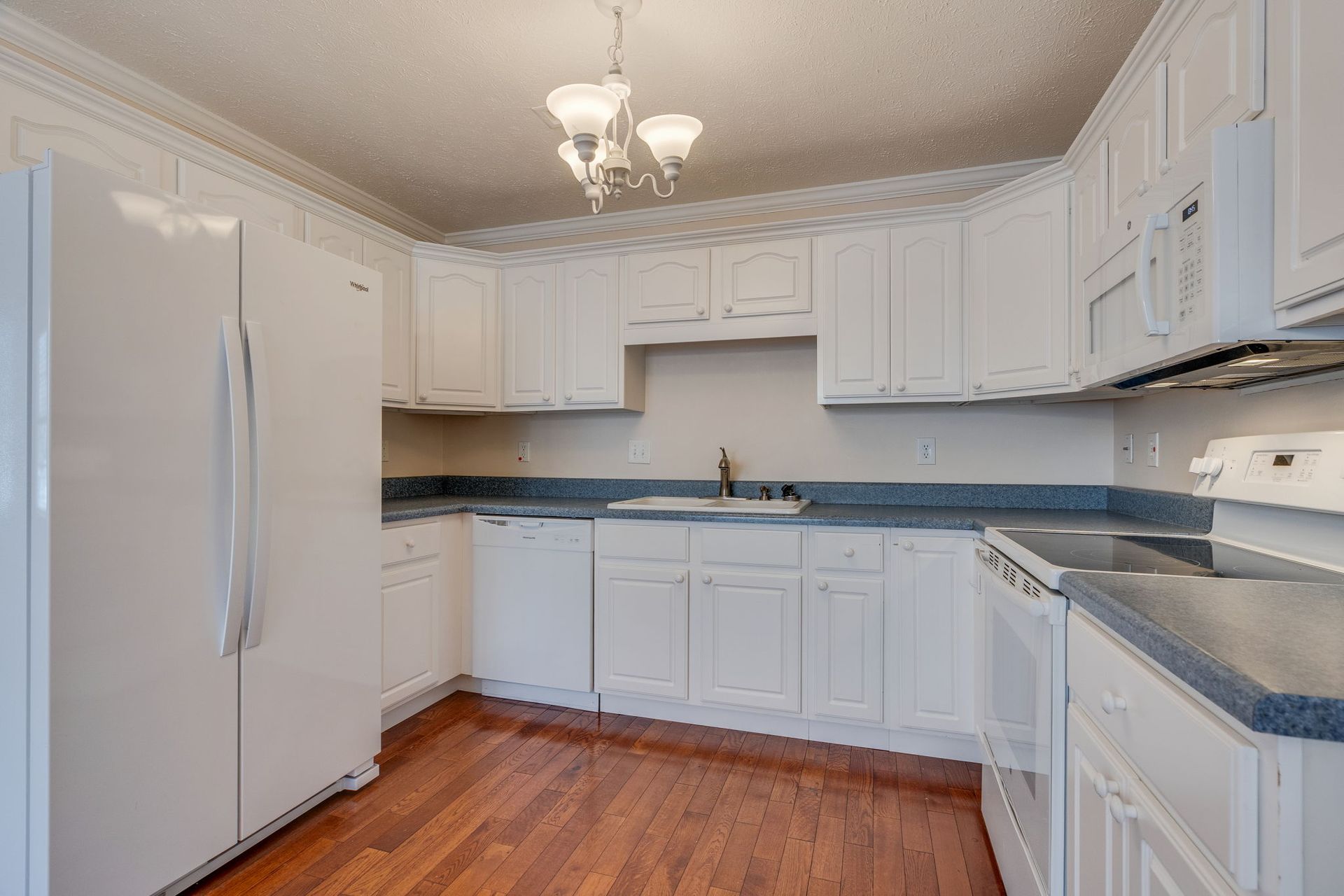 A kitchen with white cabinets, light countertops, a white refrigerator, and warm-toned wood flooring.