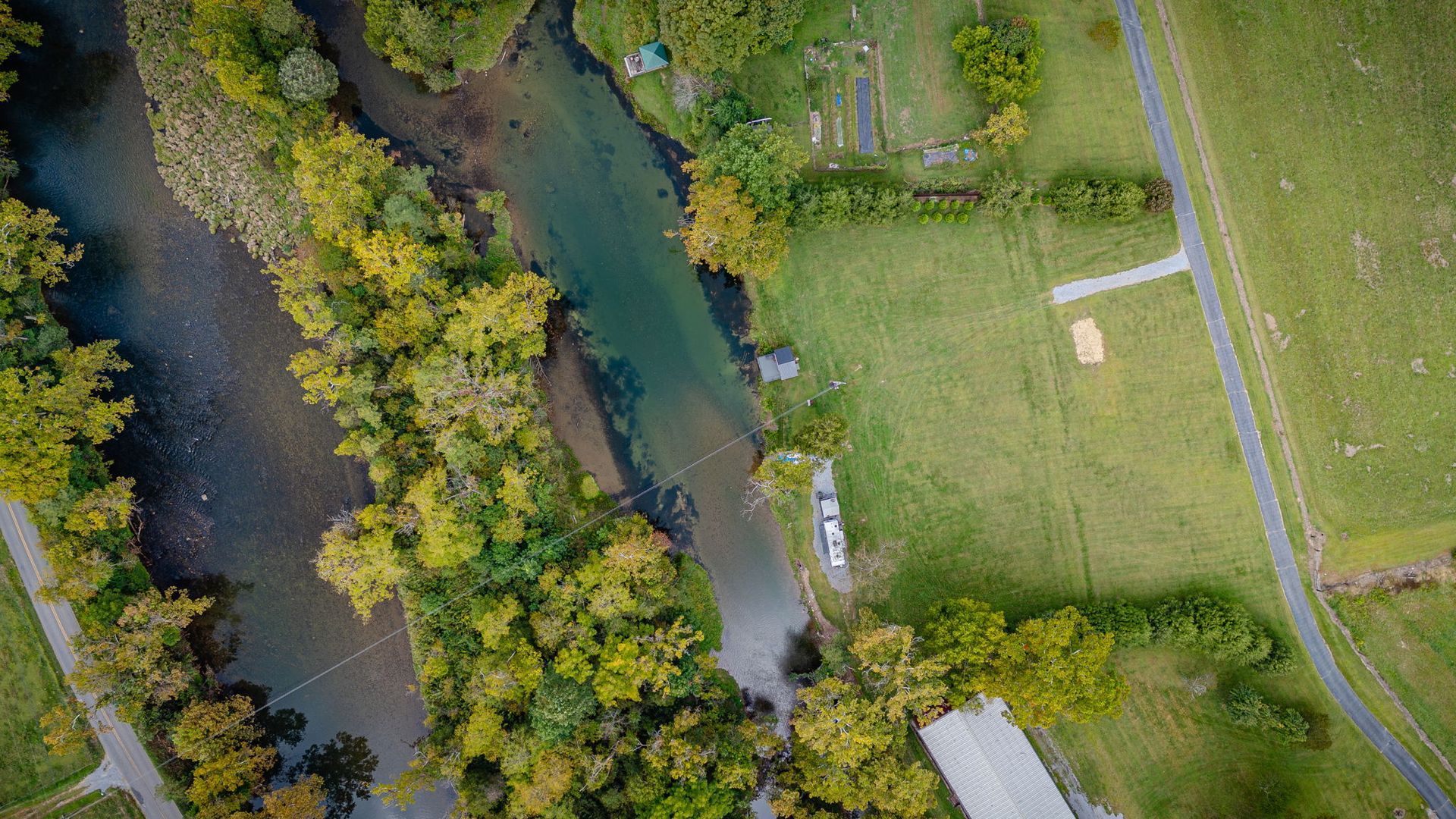 Overhead view of a river flowing through green trees and a grassy field with a road.