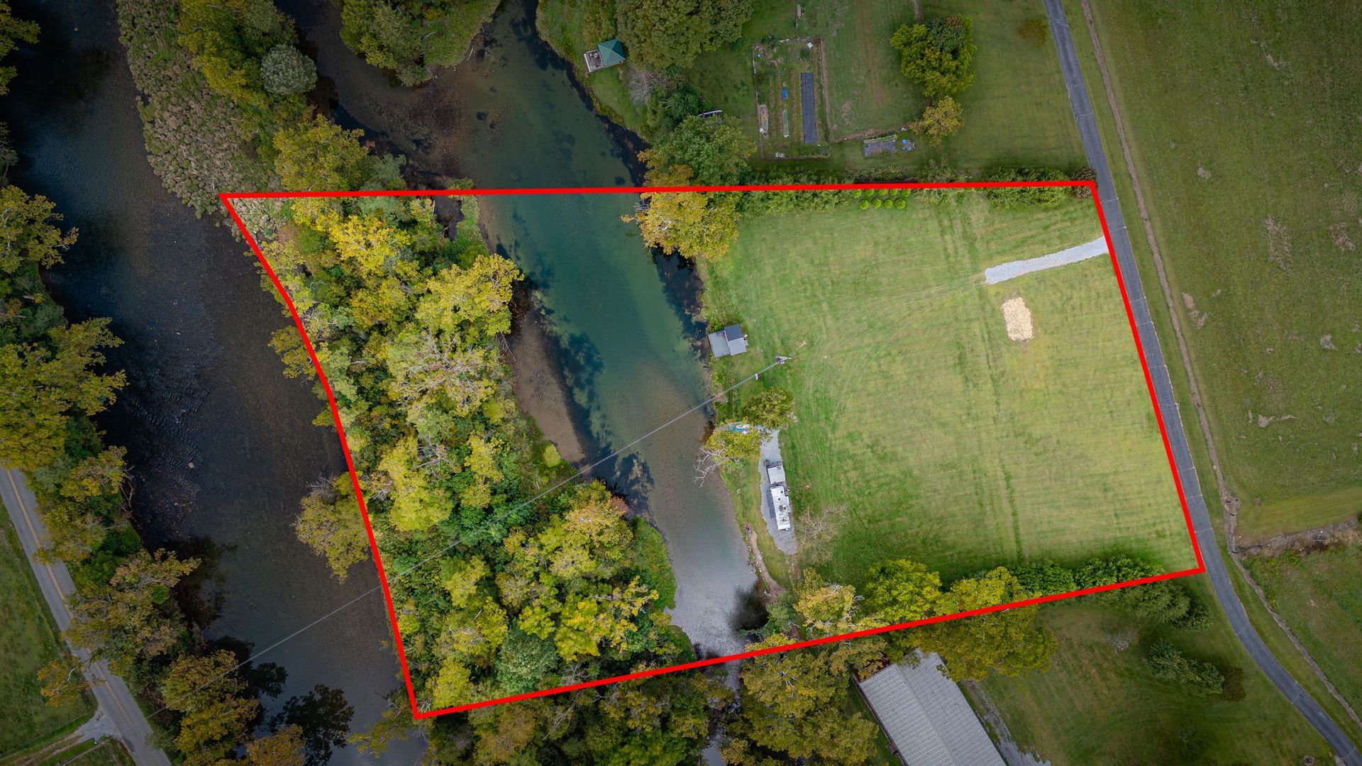 Aerial view of a grassy lot beside a river lined with trees; outlined in red.