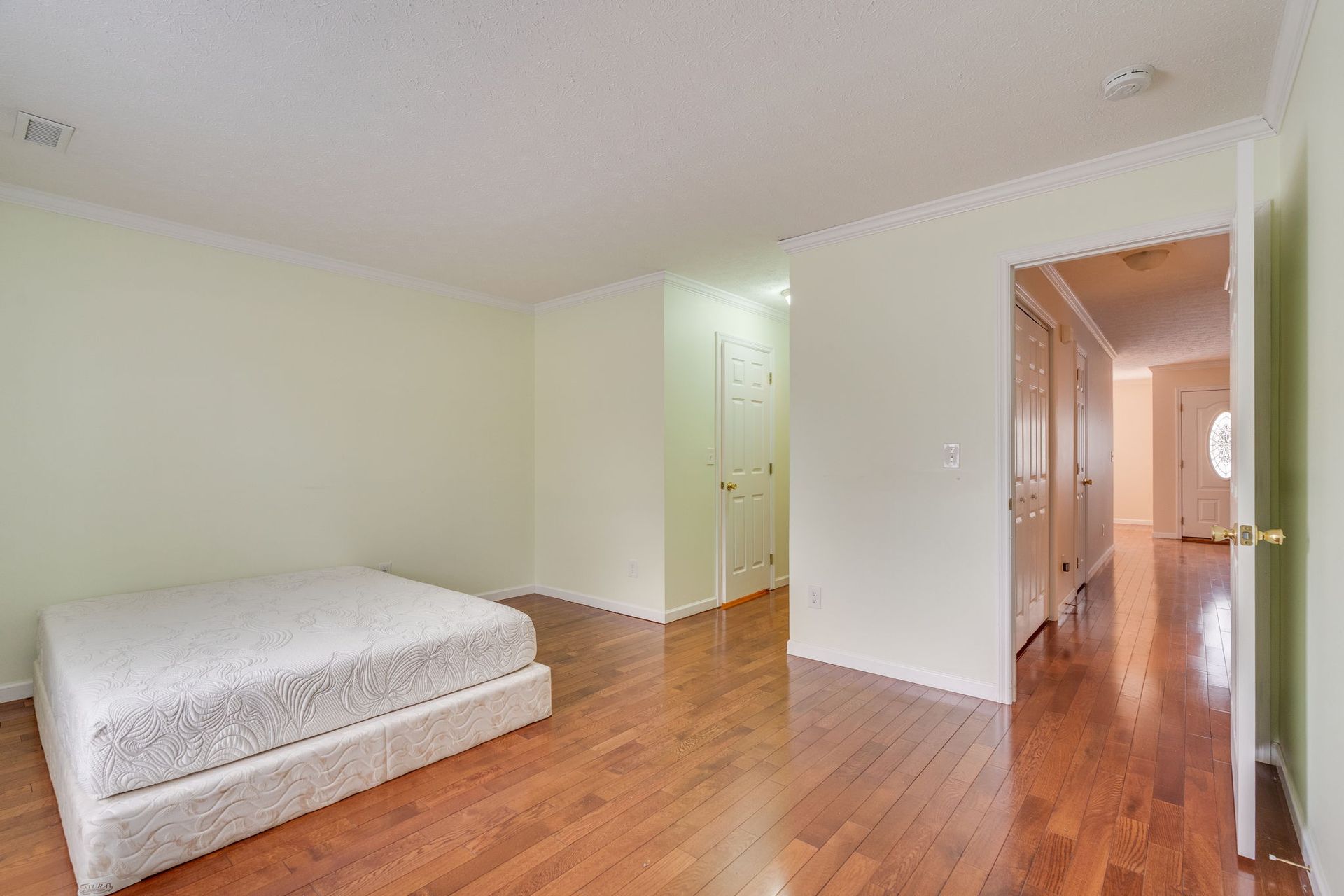 An unfurnished bedroom with a white mattress on a low base, light-colored walls, and glossy hardwood floors.