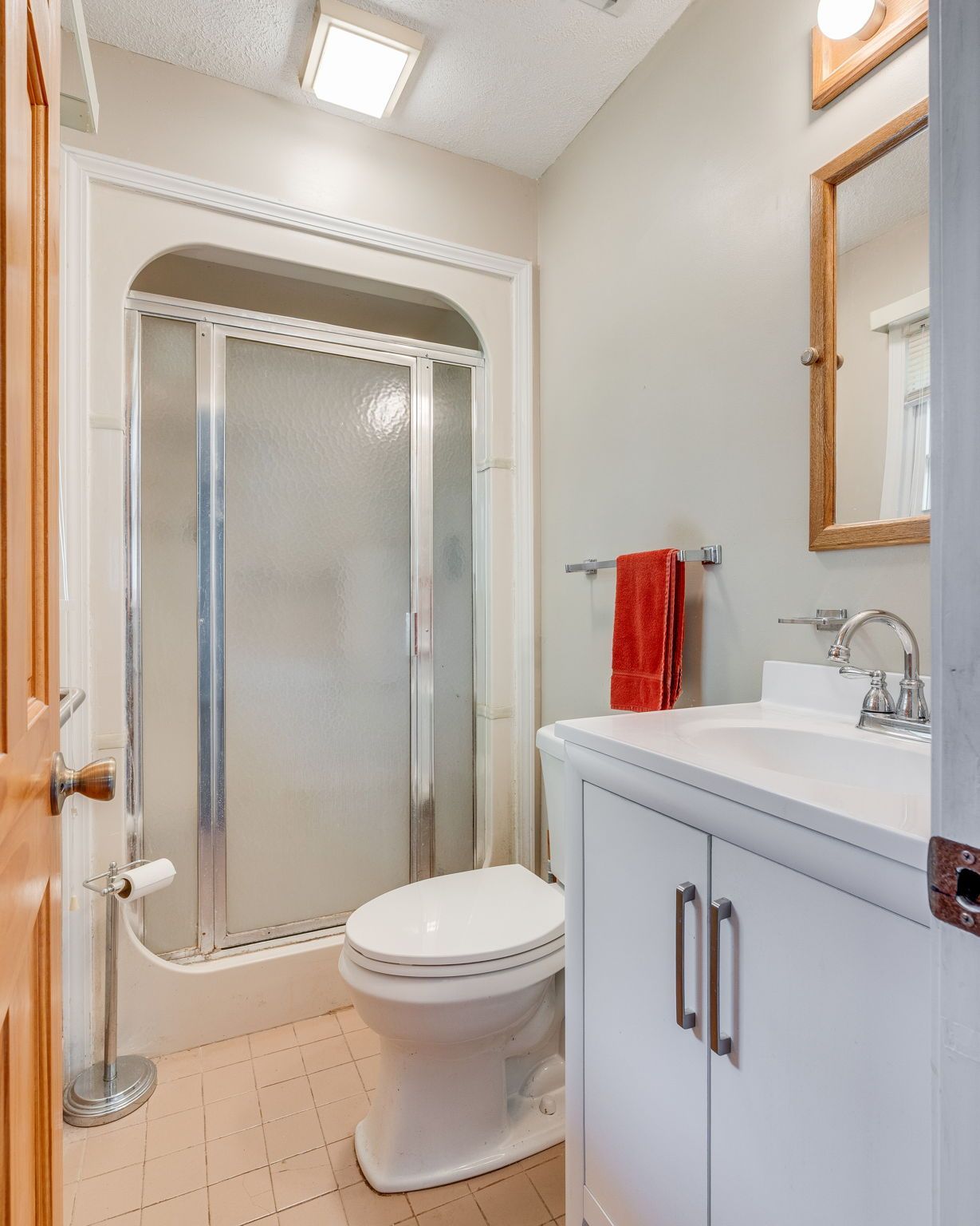 A small bathroom featuring a walk-in shower, a white toilet, and a white vanity with a sink and wooden-framed mirror.