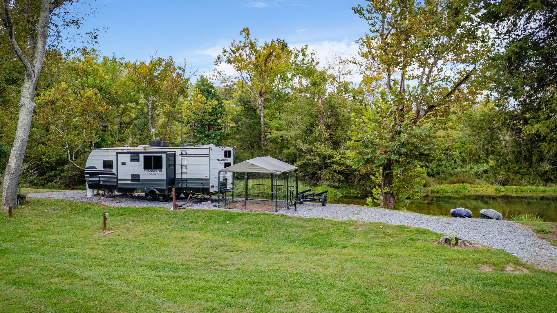 RV parked near a grassy area, gravel path, and trees near a body of water.