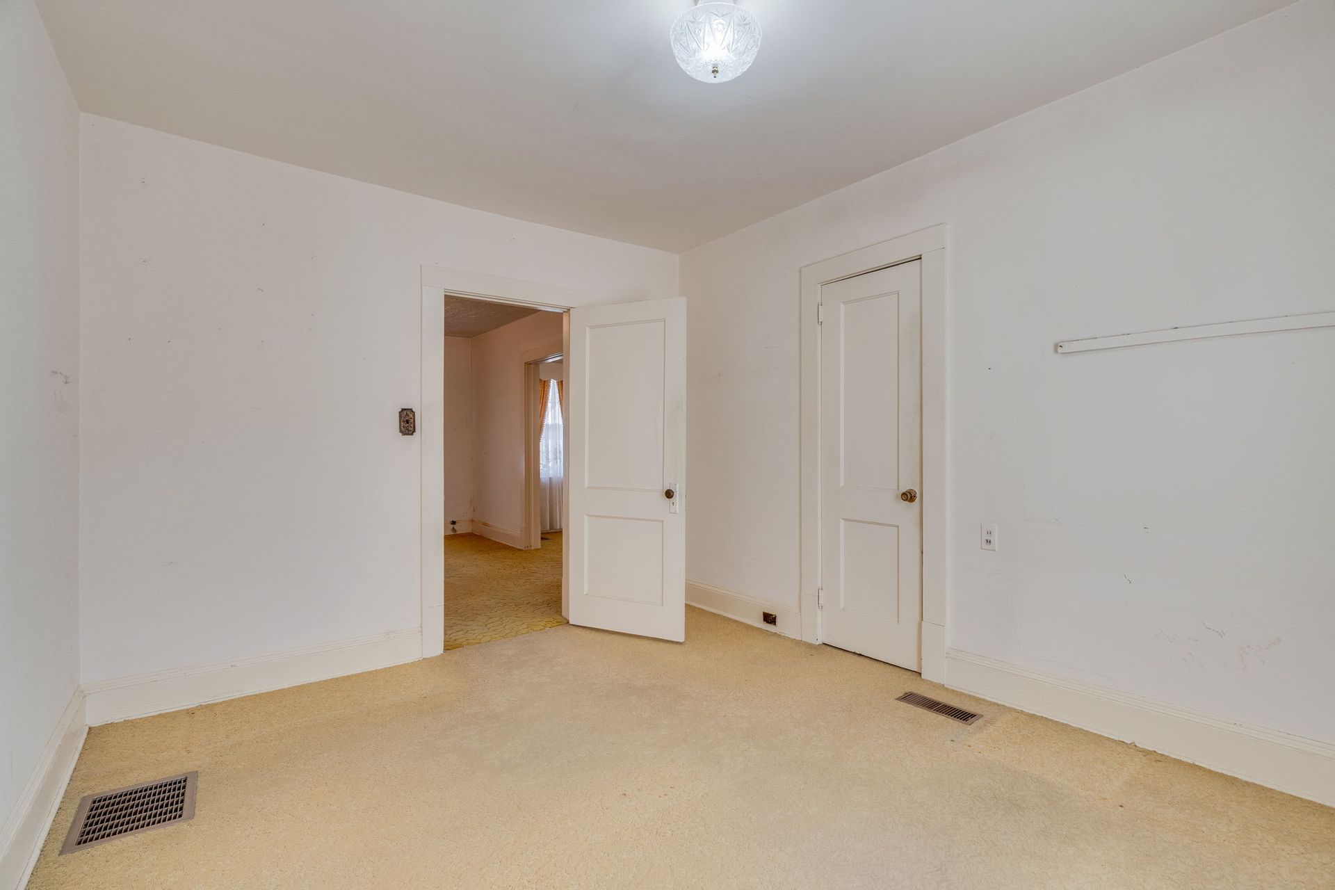 Empty room with white walls, carpet, two doors, and an open doorway.