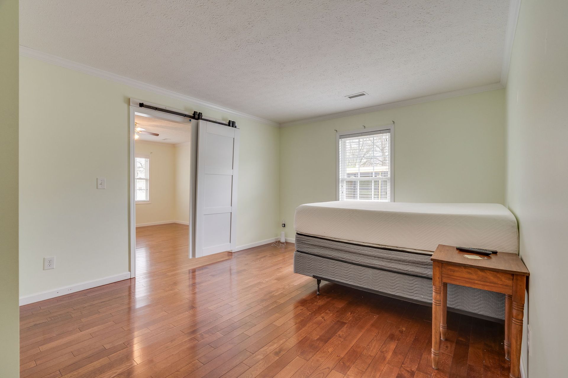 A bedroom with hardwood floors, light walls, a twin bed, a wooden side table, and a sliding white barn door.