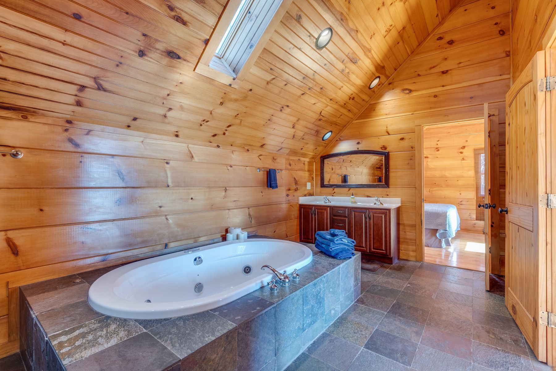 Bathroom with wooden walls, oval jacuzzi tub, vanity, and open doorway.