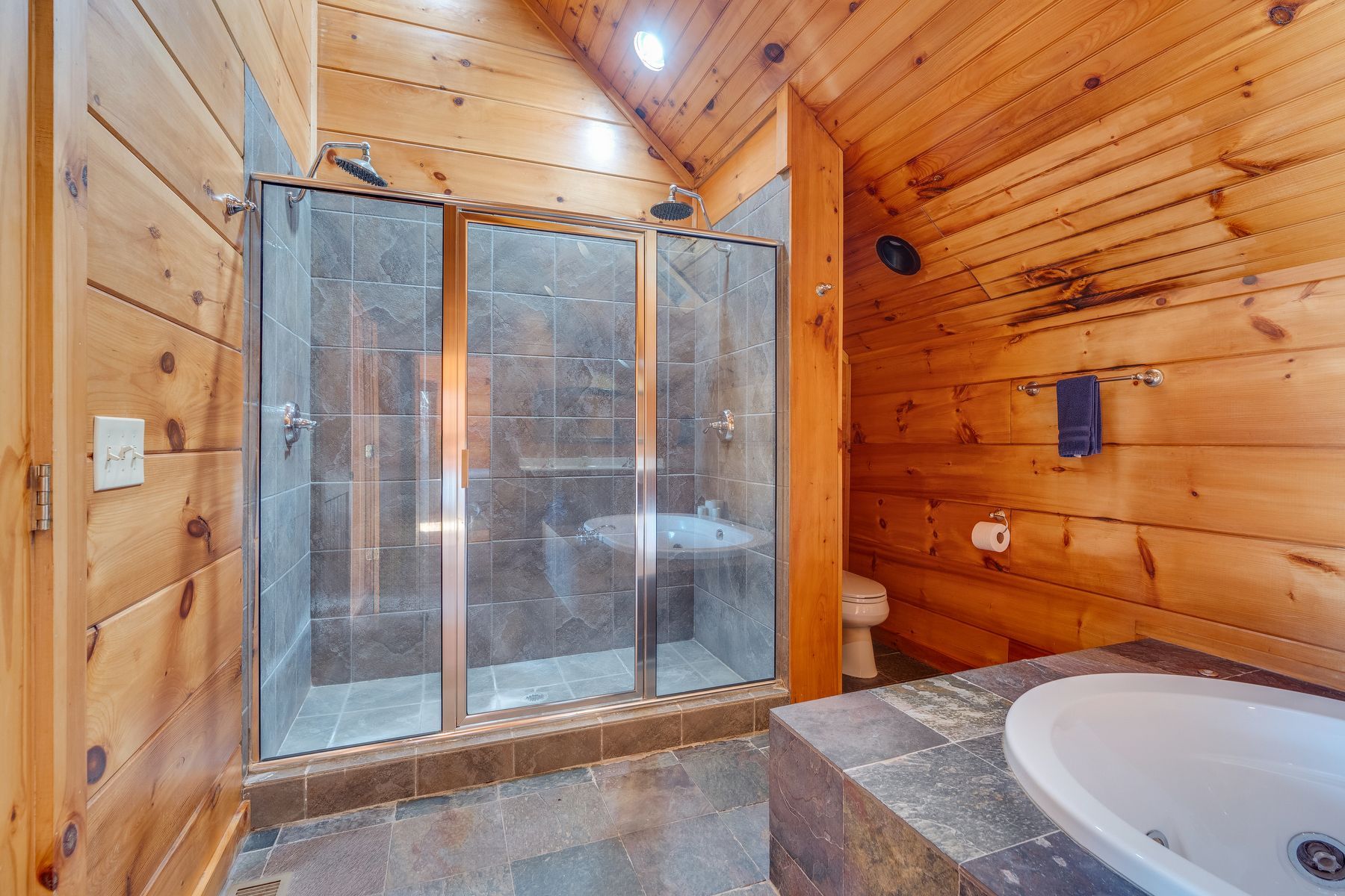 Bathroom with wooden walls, glass shower, white sink, and toilet.